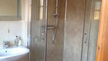 Un baño moderno con ducha de vidrio, lavamanos pedestal y un espejo.