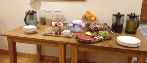 A wooden table with various food items, condiments, and drinks, suggesting a breakfast or snack setup.