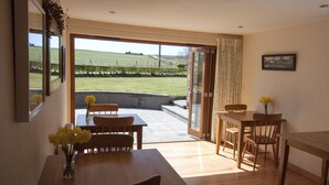 A dining area with a table and chairs, a vase with flowers, and a view of a grassy field through an open door. - Chapel Of Barras Farm Bed & Breakfast (Stonehaven)