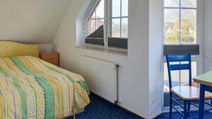 Een slaapkamer met een bed, een raam met zonwering, een radiator en een bureau met stoel.