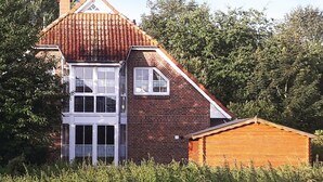 Een twee verdiepingen tellend huis met een rood pannendak, een bakstenen gevel en een houten uitbouw.