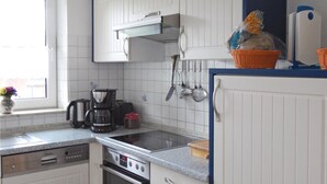 Een keuken met witte kastjes, een fornuis, een koffiezetapparaat en diverse keukengerei aan de wand.