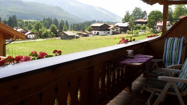 Un balcone con vista su un campo verde e case, con ringhiere in legno e un tavolo con sedie.