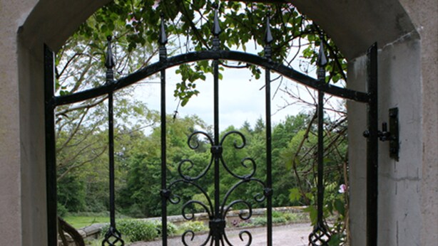 A wrought iron gate with intricate designs, leading to a garden area with a pathway and a potted plant. - Kirklands Bed & Breakfast (Melrose)