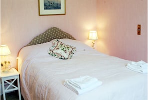 A neatly made bed with a floral pillow, two bedside lamps, and folded towels on a white nightstand. - Kirklands Bed & Breakfast (Melrose)