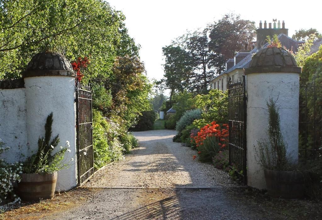 A gravel pathway leading to a gated entrance with a white building in the background.
