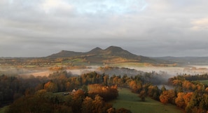 A panoramic view of a hilly landscape with a misty valley, featuring rolling hills, scattered trees, and a distant mountain range. - Kirklands Bed & Breakfast (Melrose)