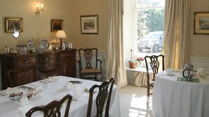 A dining area with a table set for four, wooden chairs, a chandelier, and a window with curtains. - Kirklands Bed & Breakfast (Melrose)