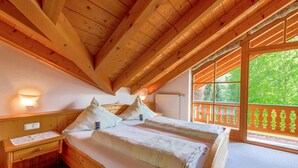 A wooden cabin bedroom with a large bed, two bedside tables, and a window with a view of greenery. - Vacation apartment 3 for 2 persons, 50 sqm, 1 bedroom and balcony (Oberwössen)