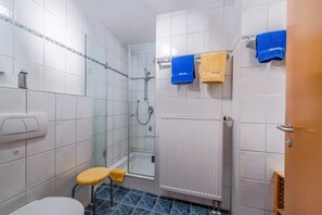Une salle de bain avec des murs carrelés de carreaux blancs, une douche en verre, des toilettes, un lavabo et un porte-serviettes avec des serviettes bleues et jaunes.