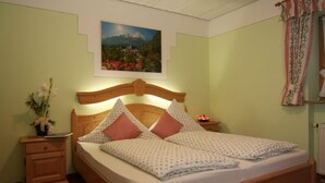 A bedroom with a wooden bed, a nightstand, a wall-mounted painting, and a window with curtains.