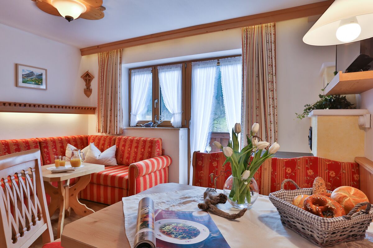 A cozy living room with a red sofa, a small table with a magazine, a vase with flowers, and a basket of bread.