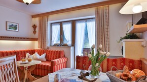 A cozy living room with a red sofa, a small table with a magazine, a vase with flowers, and a basket of bread.