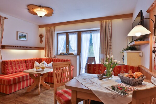 Ein gemütliches Zimmer mit einer rot gestreiften Couch, einem Holzesstisch mit weißer Tischdecke und einem Fenster mit Vorhängen.