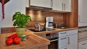 A modern kitchen with white cabinets, a wooden countertop, a coffee maker, and a stove.
