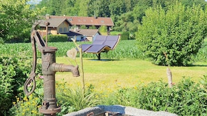 A rustic outdoor setting with a vintage water pump, a wooden chair, and a sun lounger.