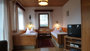 A cozy room with two wooden beds, a television on a wooden stand, and a window with curtains.