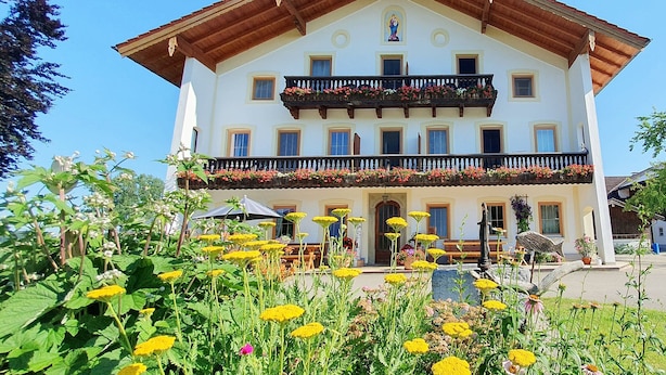 A two-story building with a balcony, surrounded by a garden with various flowers.