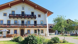A multi-story building with a balcony adorned with flowers, a covered outdoor seating area, and a garden in front.