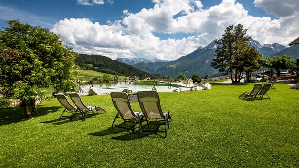 Un espacio al aire libre con césped, sillones de descanso y vistas a montañas y un lago.