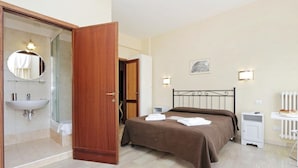 Ein Schlafzimmer mit Bett, Nachttisch, Spiegel, Waschbecken und Dusche.