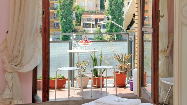 Ein Balkon mit Blumentöpfen, einem kleinen Tisch und Blick auf Gebäude.