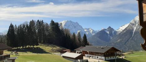 A mountain lodge with a view of snow-capped peaks, surrounded by trees and a well-maintained lawn.