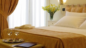Habitación de hotel con cama, mesita de noche con una bandeja de comida y dos vasos de agua, un jarrón con flores amarillas y una lámpara en la pared.