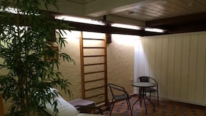 Een kleine kamer met een bed, een stoel, een tafel en een kamerplant.