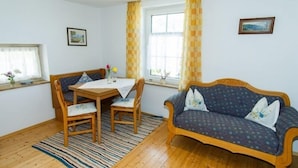 Une pièce comprenant une table à manger en bois, deux chaises, un canapé bleu avec des coussins à motifs et un tapis rayé.