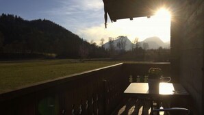 Un balcone con tavolo e sedie, vista su un prato e montagne.
