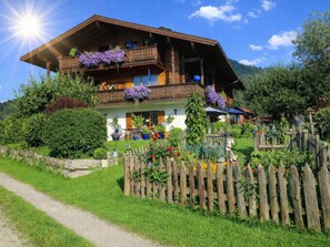 A wooden chalet with a balcony, surrounded by a garden and a wooden fence.