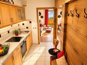 Una cocina con armarios de madera, salpicadero de azulejos y vistas a una sala de estar con sofá y cortinas rojas.