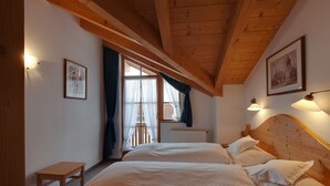 Un dormitorio con dos camas, vigas de madera, una ventana con cortinas e iluminación en la pared.