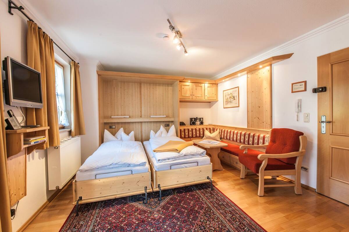 A compact hotel room with two single beds, a small seating area, a TV, and wooden furniture.
