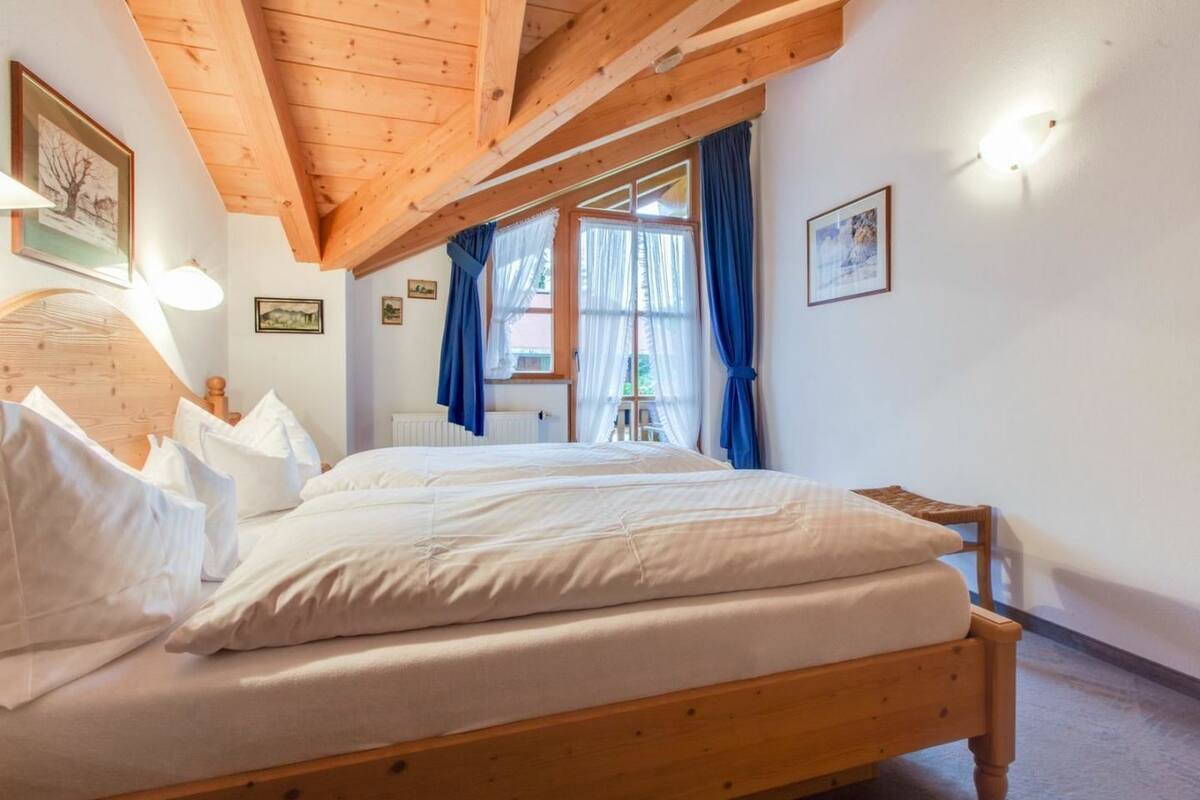 A bedroom with a wooden bed, white bedding, a wooden headboard, a window with blue curtains, and a radiator.