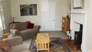 A living room with a sofa, a small table, a rug, a fireplace, and a door. - Kirklands Cottages (Melrose)