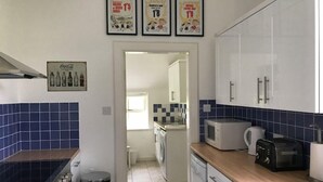 A kitchen with white cabinets, a microwave, a toaster, and a sink. There are three framed posters on the wall and a Coca-Cola sign. - Kirklands Cottages (Melrose)
