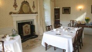 A dining room with a fireplace, a table set for a meal, and a mirror above the mantel. - Kirklands Cottages (Melrose)