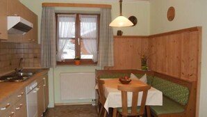 A compact kitchen with a dining area, including a table with chairs and a bench. - Ferienwohnung Jenner für 1-3 Pers., ca. 34 qm, Schlafzimmer, Wohnküche, Balkon (Bischofswiesen)