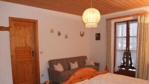 A bedroom with a wooden bed, a wooden wardrobe, a sofa, and a window with curtains. - Ferienwohnung Jenner für 1-3 Pers., ca. 34 qm, Schlafzimmer, Wohnküche, Balkon (Bischofswiesen)