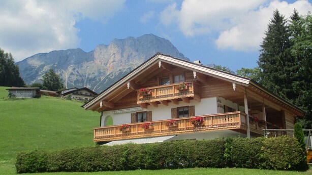 Een houten chalet met een balkon, gelegen tegen een bergachtige achtergrond.