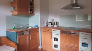 Een kleine keuken met houten kastjes, een inbouwoven, een koffiezetapparaat en een roestvrijstalen afzuigkap.
