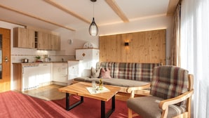 Ein gemütliches Wohnzimmer mit einer Couch, einem Holztisch und einer Küche im Hintergrund.