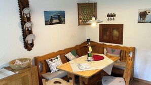 A cozy dining area with a wooden bench, a table with a red placemat, and a bottle of wine. - Ferienwohnung "Beste Laune" (Reit im Winkl)