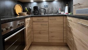 A compact kitchen with wooden cabinets, a built-in oven, and a coffee maker. - Ferienwohnung "Beste Laune" (Reit im Winkl)