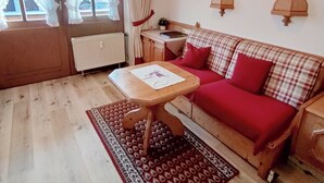 Een gezellige woonkamer met een houten vloer, een rode bank, een houten tafel en een raam met gordijnen.