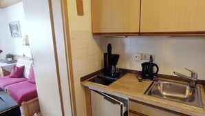 Een compacte keuken met houten kastjes, een spoelbak, een koffiezetapparaat en een kleine koelkast.