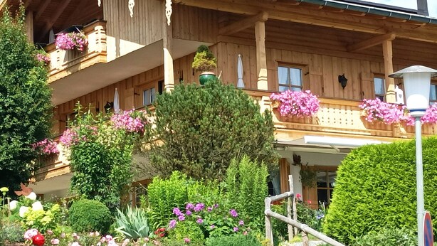 Een traditionele houten chalet met balkon, omringd door weelderige tuinen en bloeiende planten.