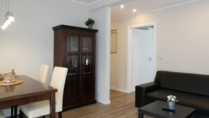 A modern living room with a dining area, a dark wooden cabinet, a black sofa, and a small table with a plant. - Vacation apartment by the Baltic Sea - Apartment Kapitän 3 (Zinnowitz)
